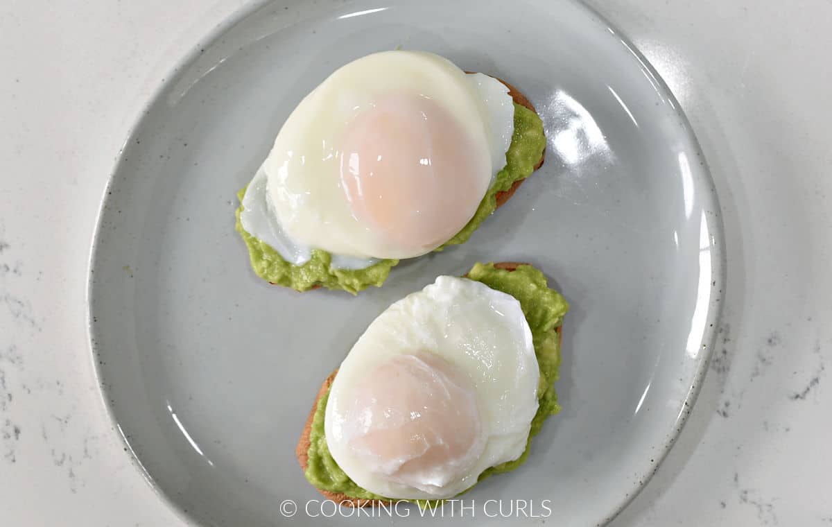 Two poached eggs on top of mashed avocado and two sweet potato toasts on a small plate.