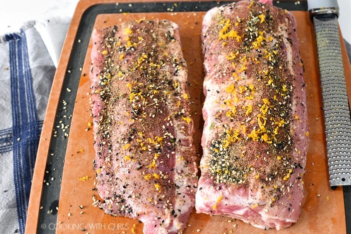 Two racks of pork ribs covered in seasoning laying on a plastic cutting board