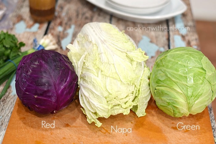 Red, Napa, and green cabbage on a cutting board.