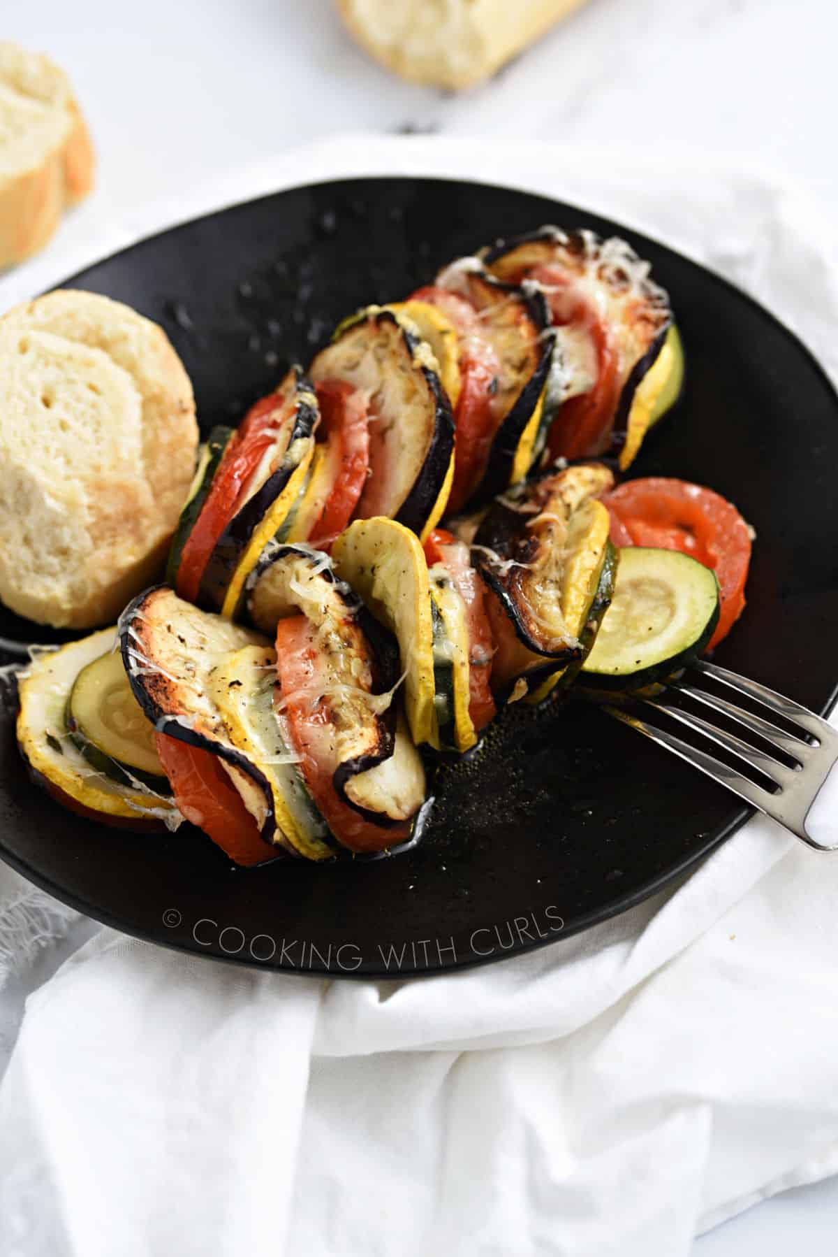 Vegetable Tian on a black plate with a slice of bread. 
