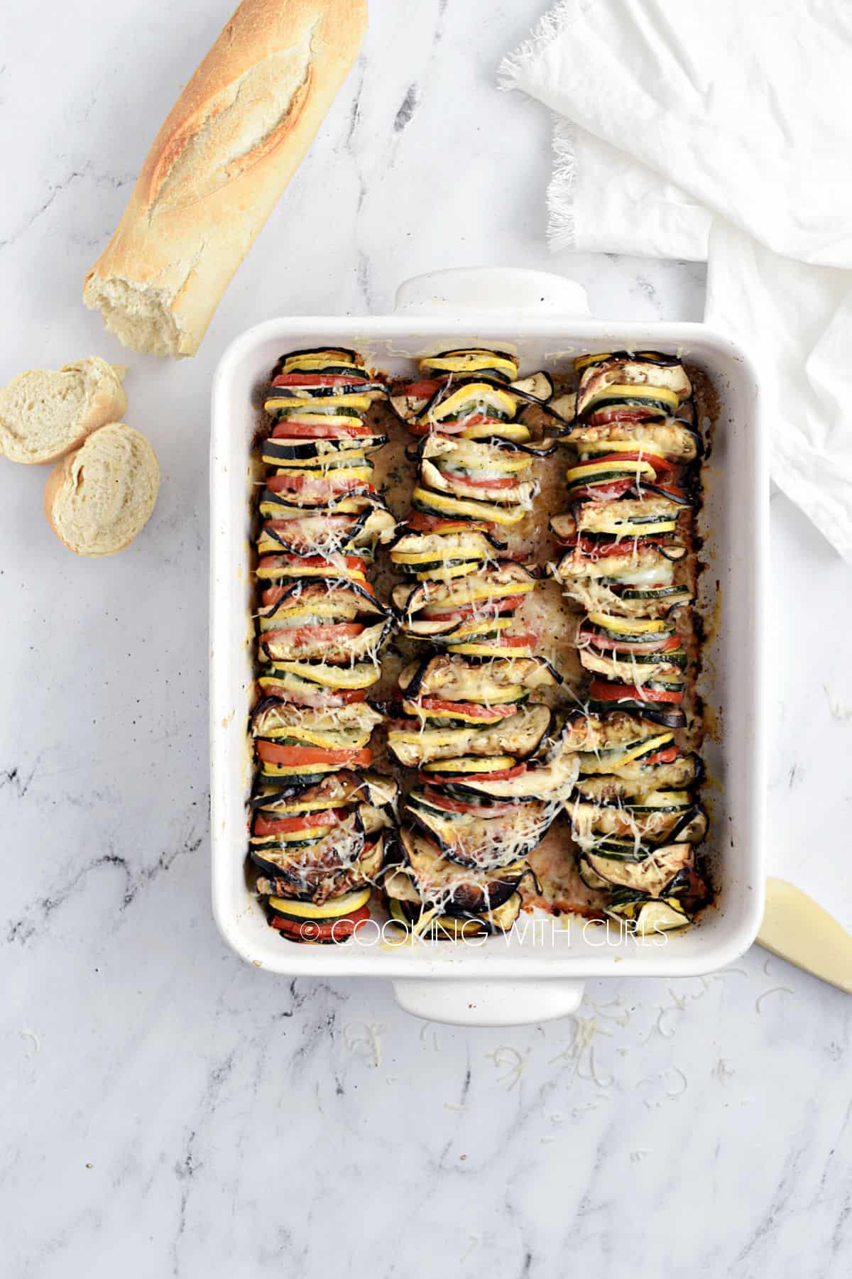 Vegetable Tian Recipe in a white baking dish with a loaf of bread in the background. 