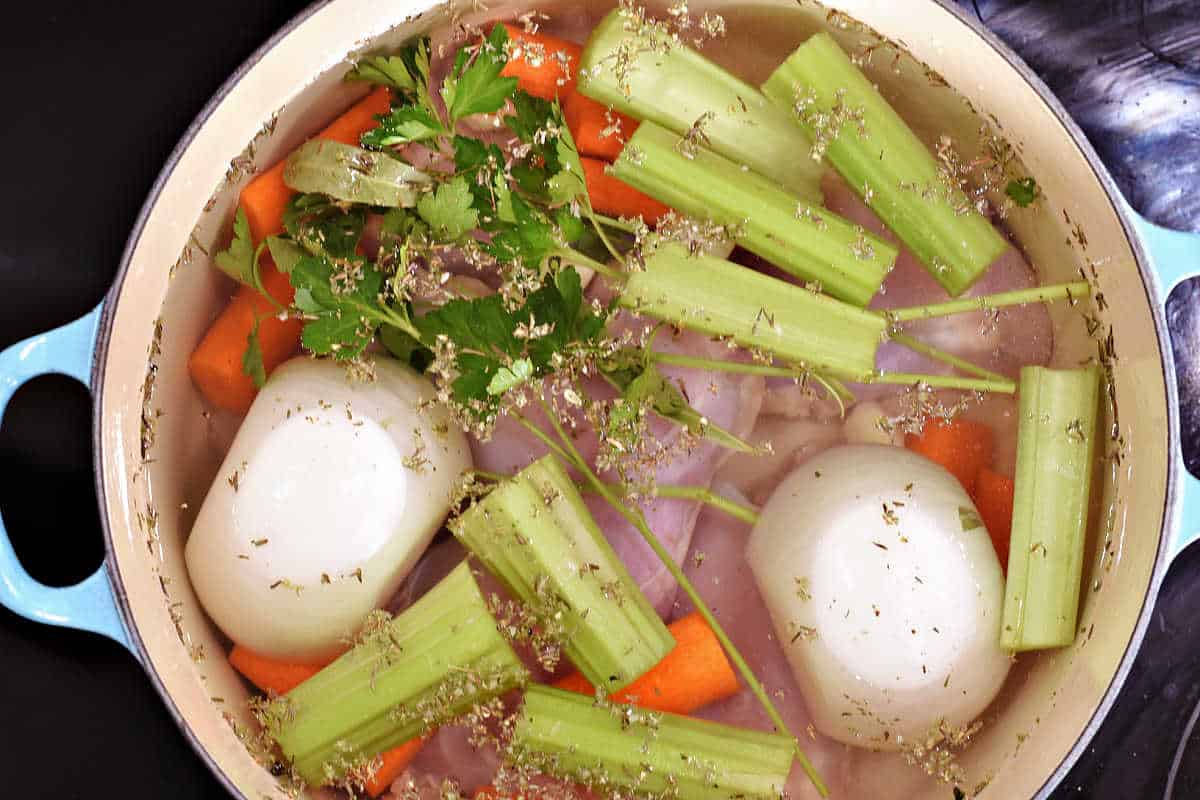 Water, onion halves, chopped celery and carrots, chicken thighs, garlic, and seasonings in a Dutch oven.