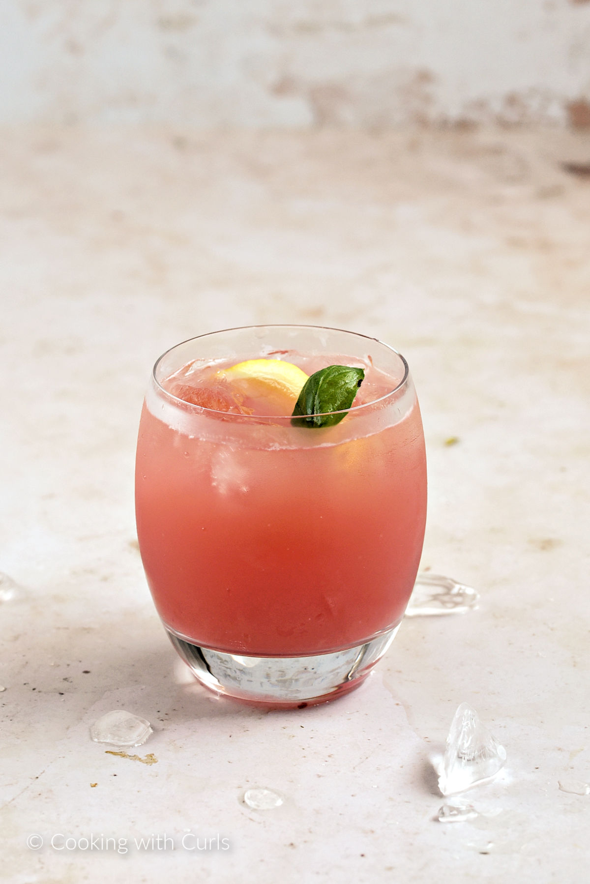 A glass of watermelon basil lemonade with a lemon wedge and basil leaf.