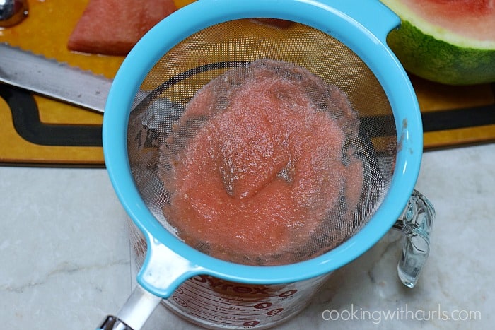Watermelon pulp in a strainer over a large glass measuring cup.