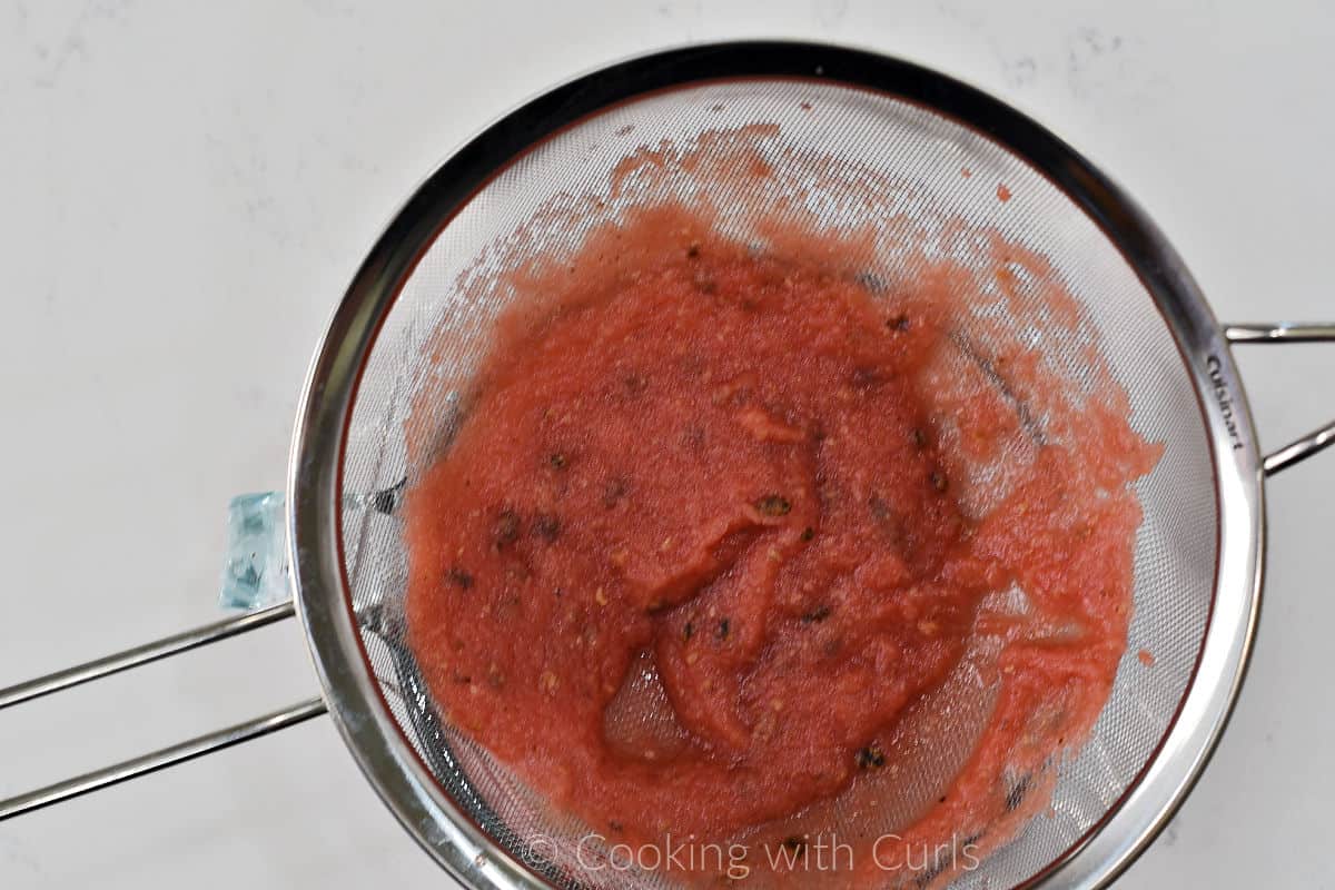 Watermelon pulp in a fine mesh strainer over a large measuring cup. 