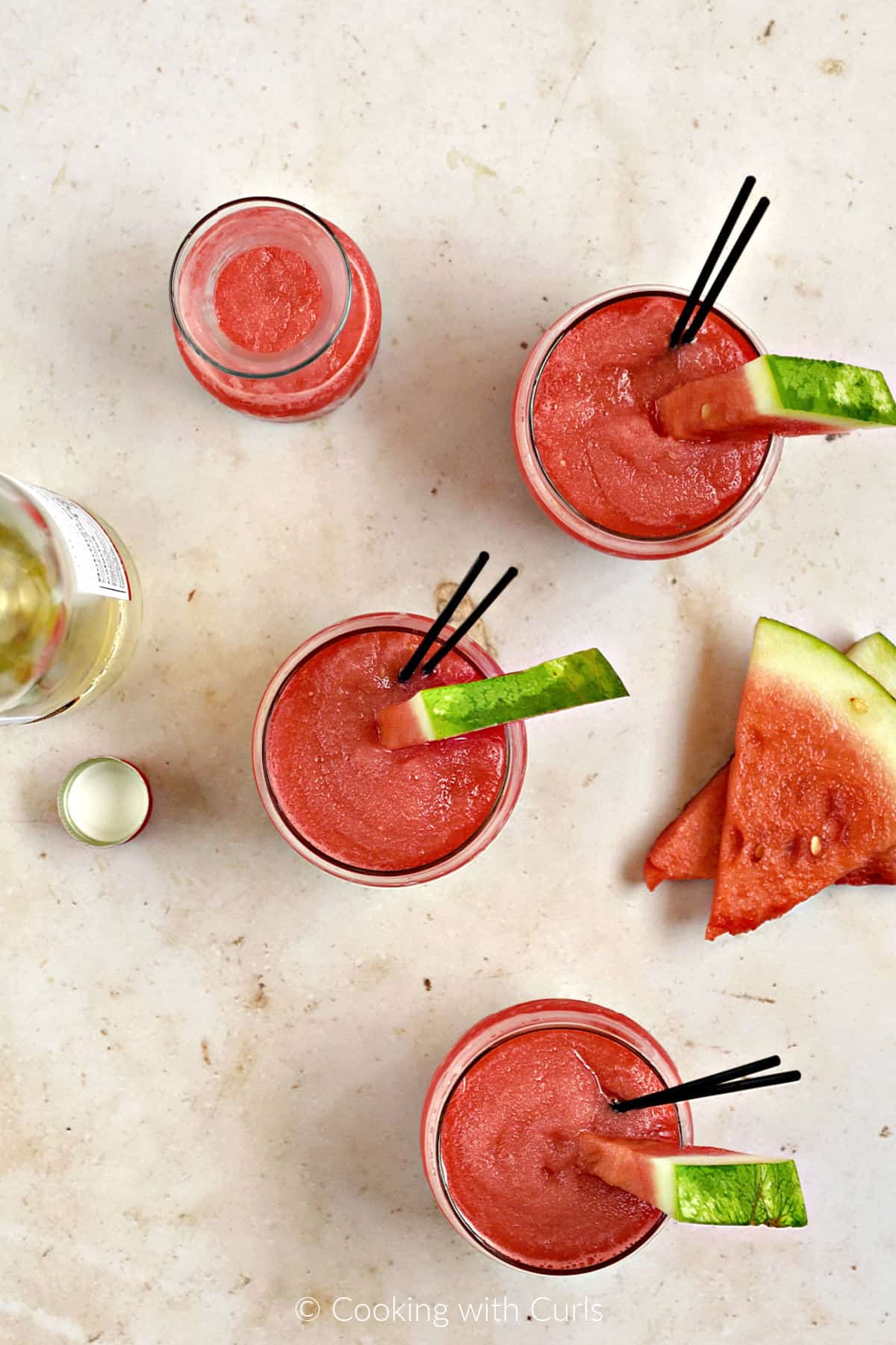 Looking down on three small glasses of frozen watermelon wine smoothie with watermelon wedges for garnish.