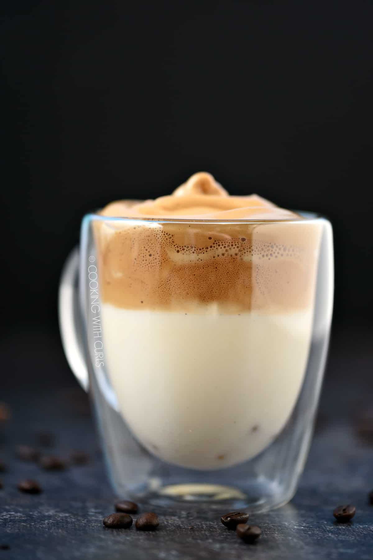 Side view of whipped dalgona coffee floating on top of milk in a clear glass mug.