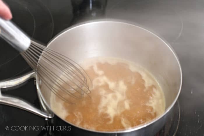 whisking the beef stock into the darkened roux in the saucepan. 