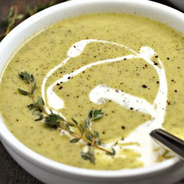 A bowl of creamy zucchini soup swirled with cream and topped with fresh thyme sprigs.