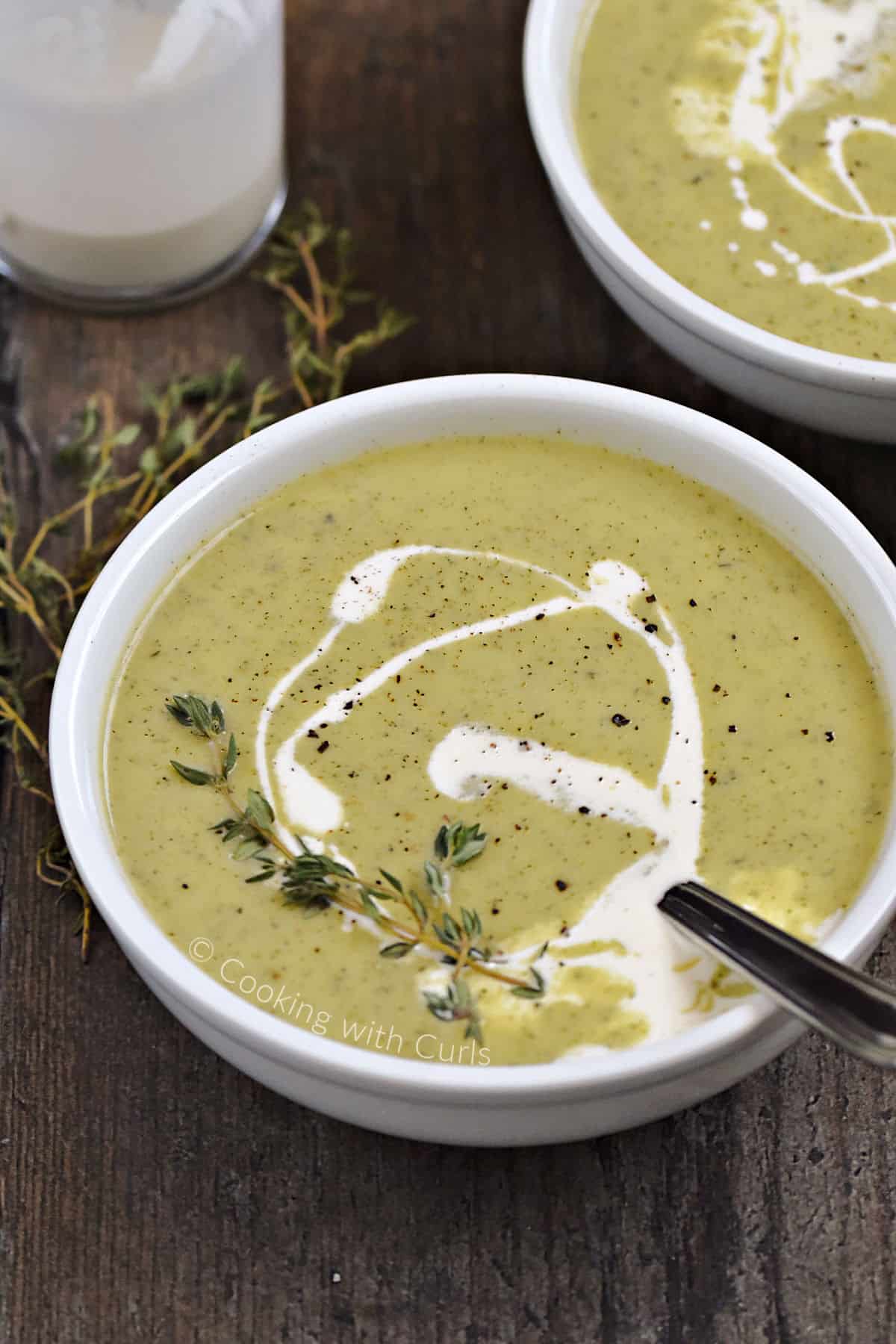 A bowl of creamy zucchini soup swirled with cream and topped with fresh thyme sprigs.