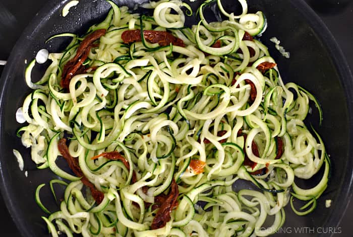 Zucchini noodles and sun-dried tomato strips in a non-stick skillet. 