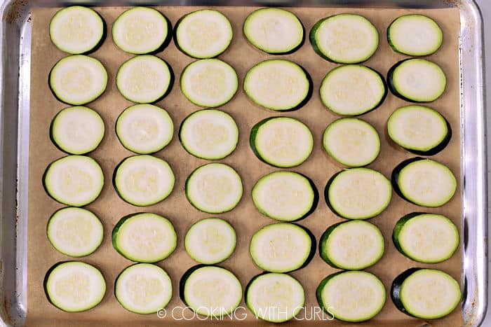 Zucchini slices on a parchment lined baking sheet. 